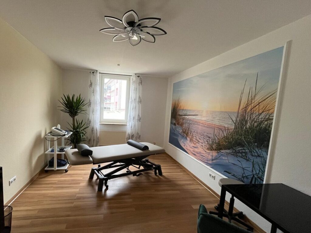 Behandlungsraum mit Therapieliege, Elektrotherapiegeraet und Strandmotiv