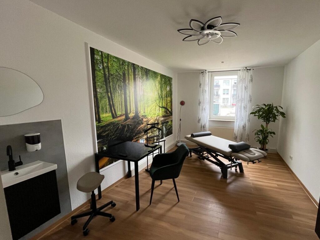 Behandlungsraum mit Therapieliege, Schreibtisch und Waldmotiv